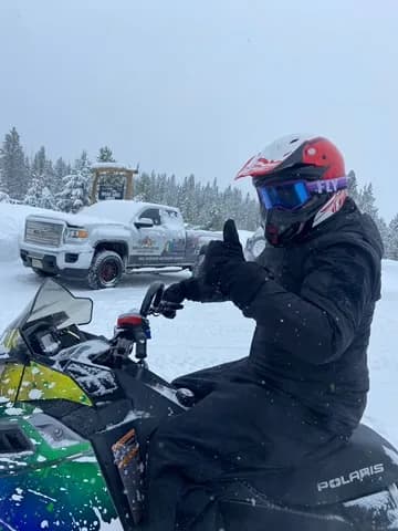 Rider giving a thumbs up on a Polaris snowmobile in fresh snow
